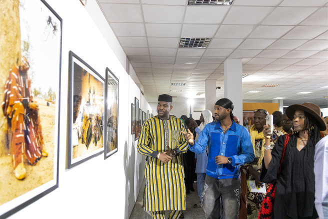 Un groupe de personnes admirant des photographies dans une galerie d'art, avec des hommes portant des vêtements traditionnels africains.
